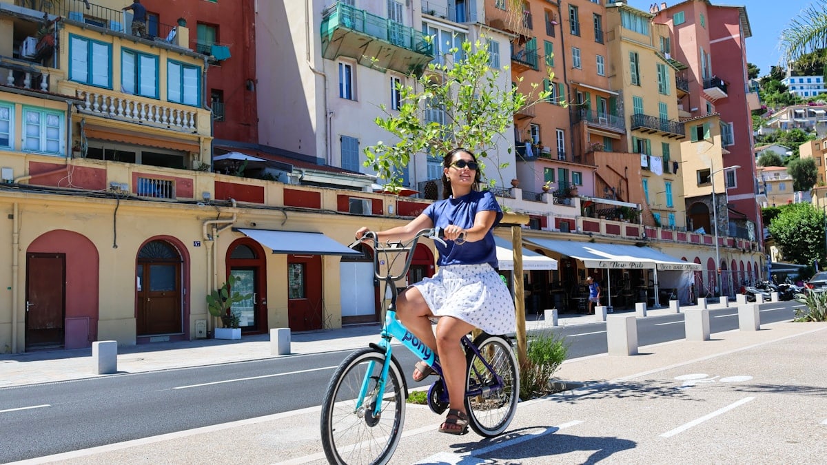 Woman rides a bicycle along a colorful waterfront street.
